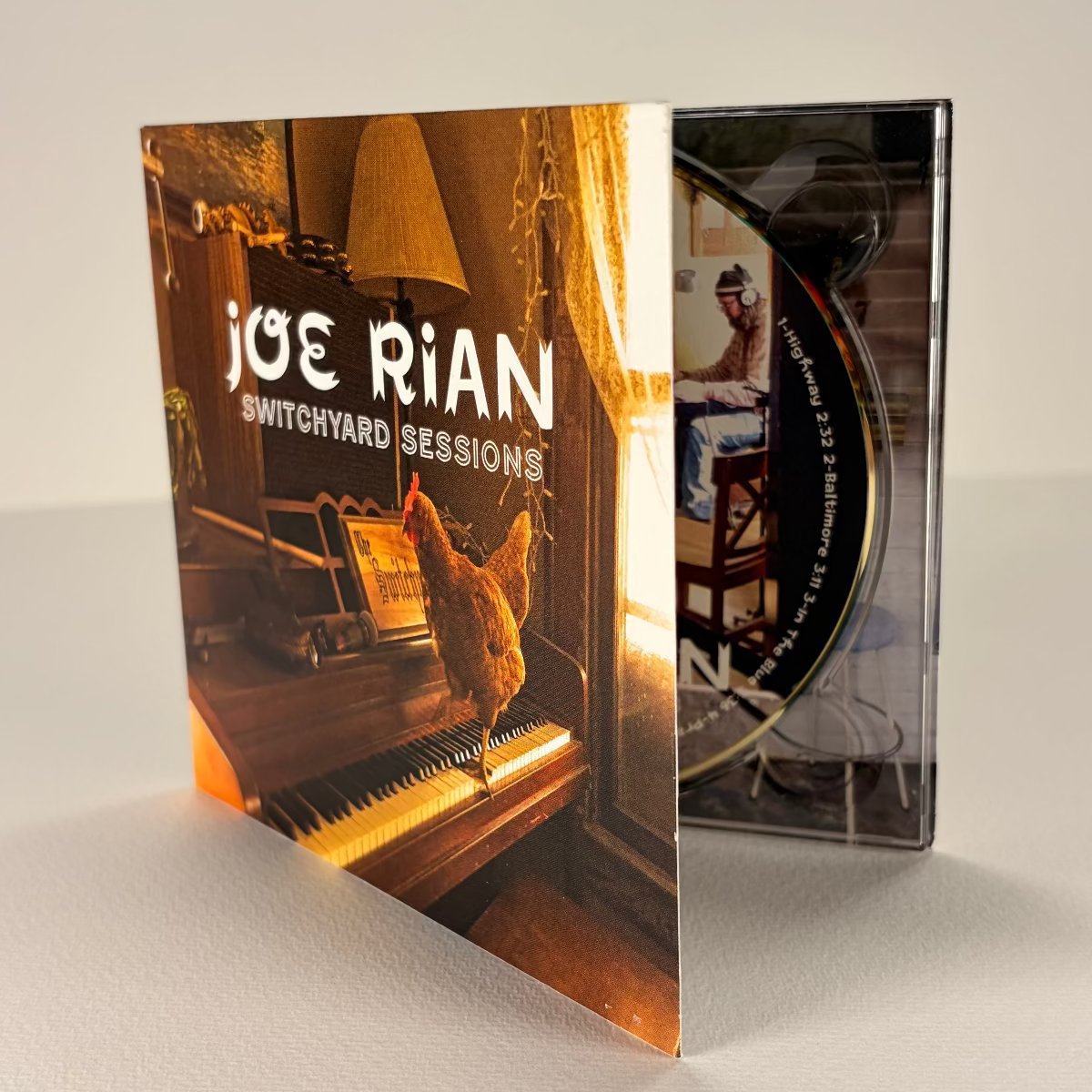 CD cover of 'Switchyard Sessions' by Joe Rian with a piano and lamp in the background.